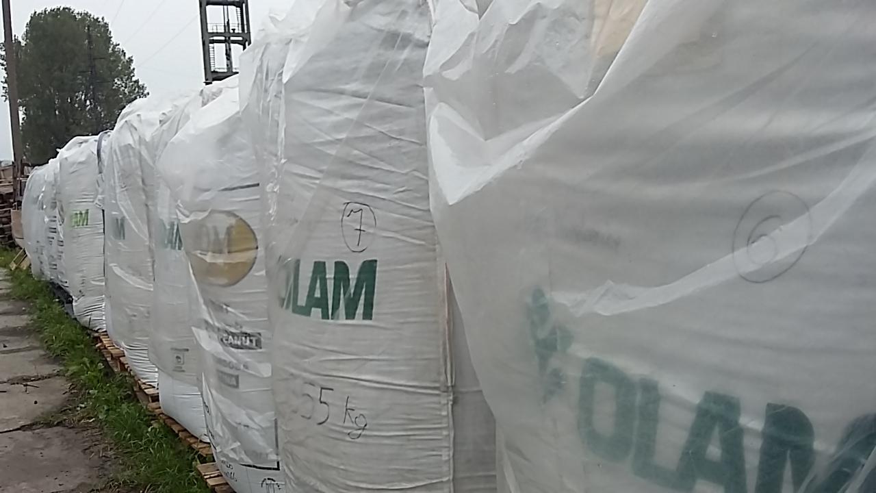 Rząd worków z nawozem firmy OLAM, ułożonych na paletach na zewnątrz, widoczne numery od 6 do 7 na workach.