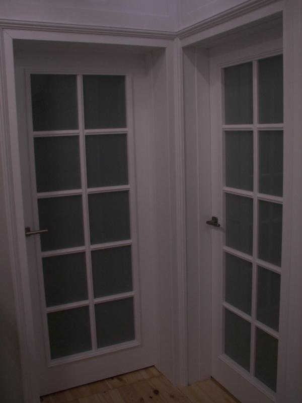 Dwa białe, przeszklone drzwi wewnętrzne z podziałami na 6 pól każde, widoczne fragmenty drewnianej podłogi.