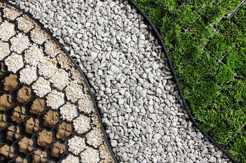 Zbliżenie na wypełnione kraty trawnikowe: z lewej ziemia i drobny kamień, pośrodku biały drobny kamień, z prawej trawa.