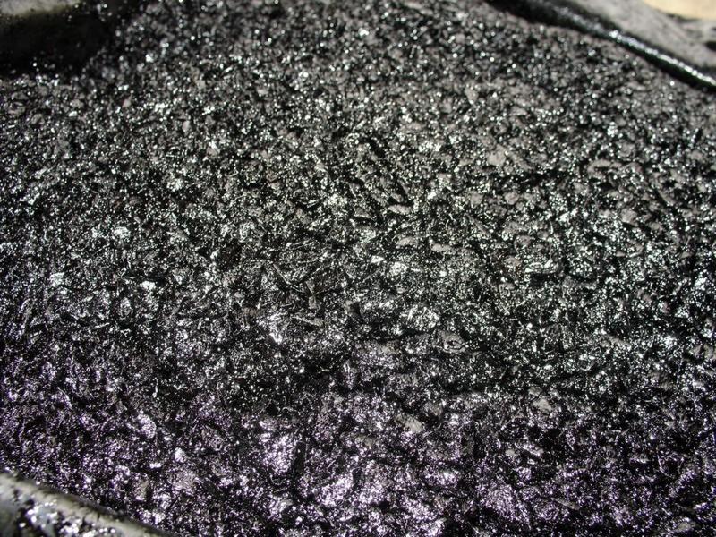 Błyszcząca, drobnoziarnista masa asfaltowa na zimno, z widocznymi refleksami światła na powierzchni.