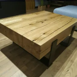 Stolik kawowy z litego drewna dębowego o wyraźnym usłojeniu i czarnych, metalowych nogach, ustawiony na parkiecie w salonie.