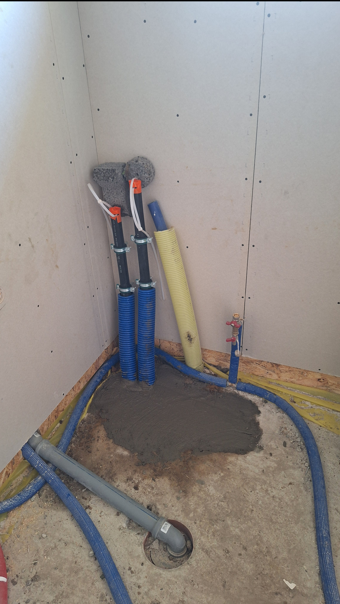 Montaż instalacji pod pompę ciepła: rury w izolacji, wylewka betonowa, widoczne elementy instalacji wodnej w surowym wnętrzu.