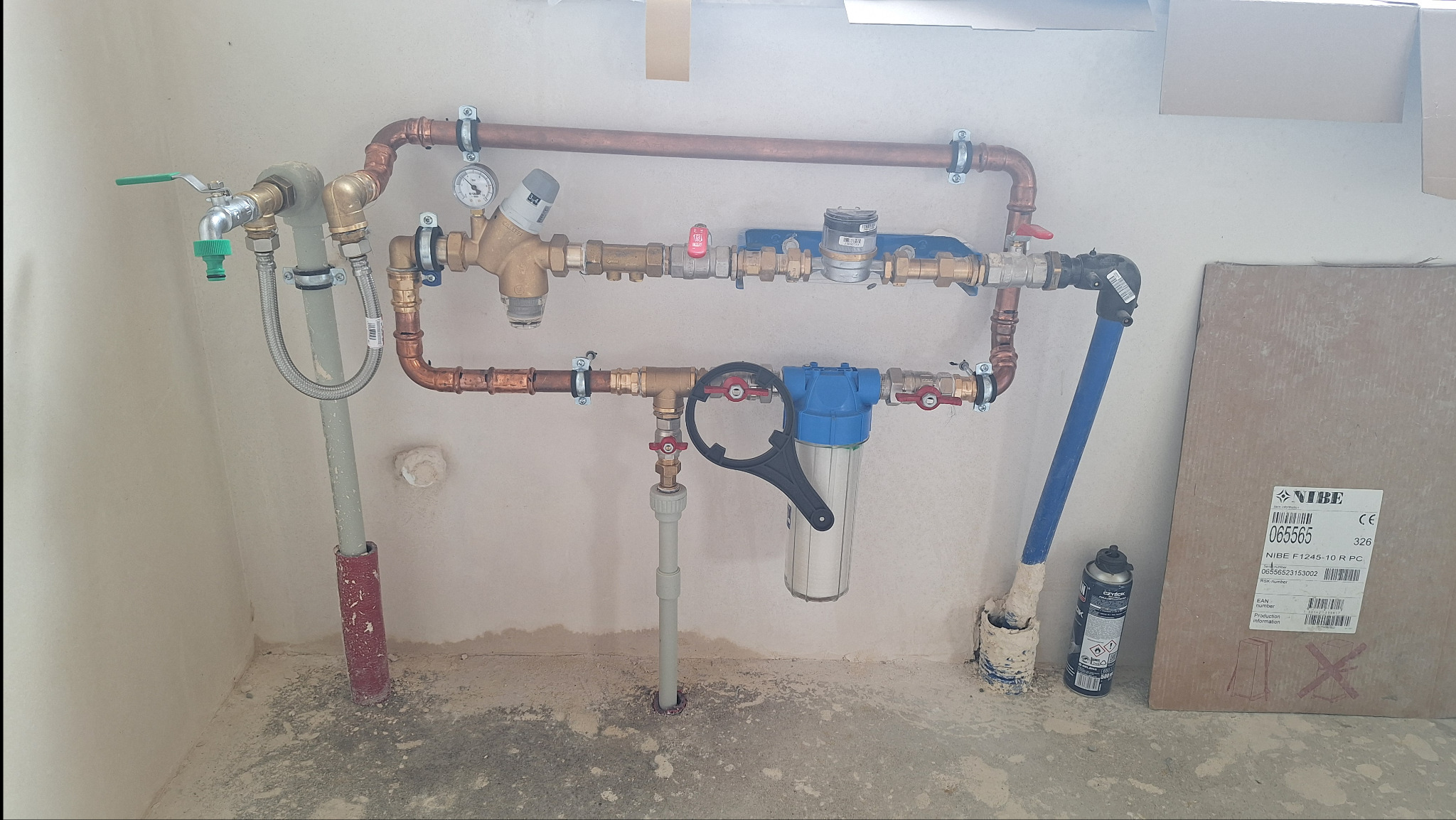 Instalacja wodna z rur miedzianych, zaworów i filtra wody, zamontowana na ścianie w surowym pomieszczeniu, widoczna skrzynka NIBE F1245-10 R PC.
