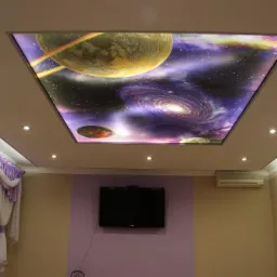 Pokój z beżowymi ścianami i sufitem z podświetlanym panelem z motywem kosmosu: planeta z pierścieniami i galaktyka spiralna.