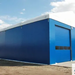 Gotowa hala magazynowa z niebieskich płyt warstwowych z bramą segmentową i białym dachem membranowym, widoczny logo firmy Fourtech.