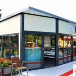 Pawilon handlowy z płyt warstwowych i aluminiową stolarką okienną, z widocznym basenem i kwiatami w donicach.