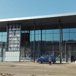 Mal-Nat - Budowa nowoczesnego budynku biurowego z przeszkloną fasadą i metalową konstrukcją, widoczne pojazdy budowlane i robotnicy.