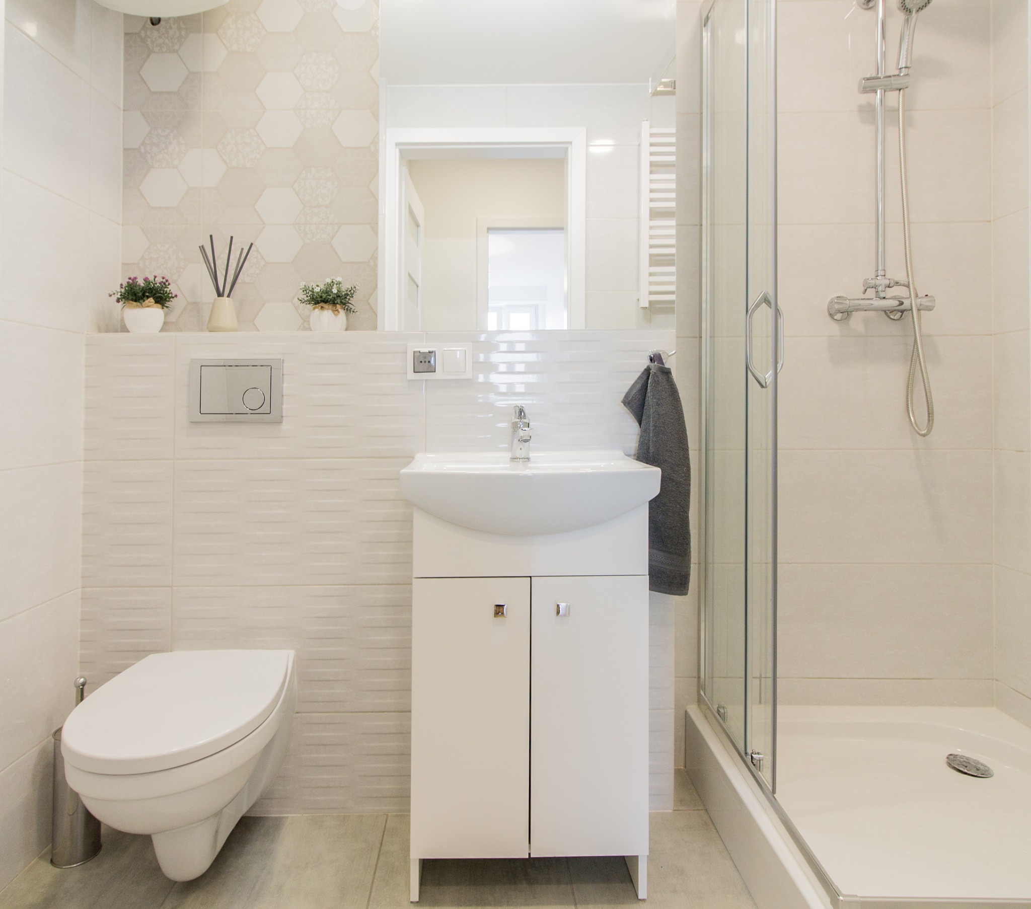 Jasna łazienka z kabiną prysznicową, umywalką z szafką, podwieszaną toaletą i dekoracyjnymi płytkami heksagonalnymi.