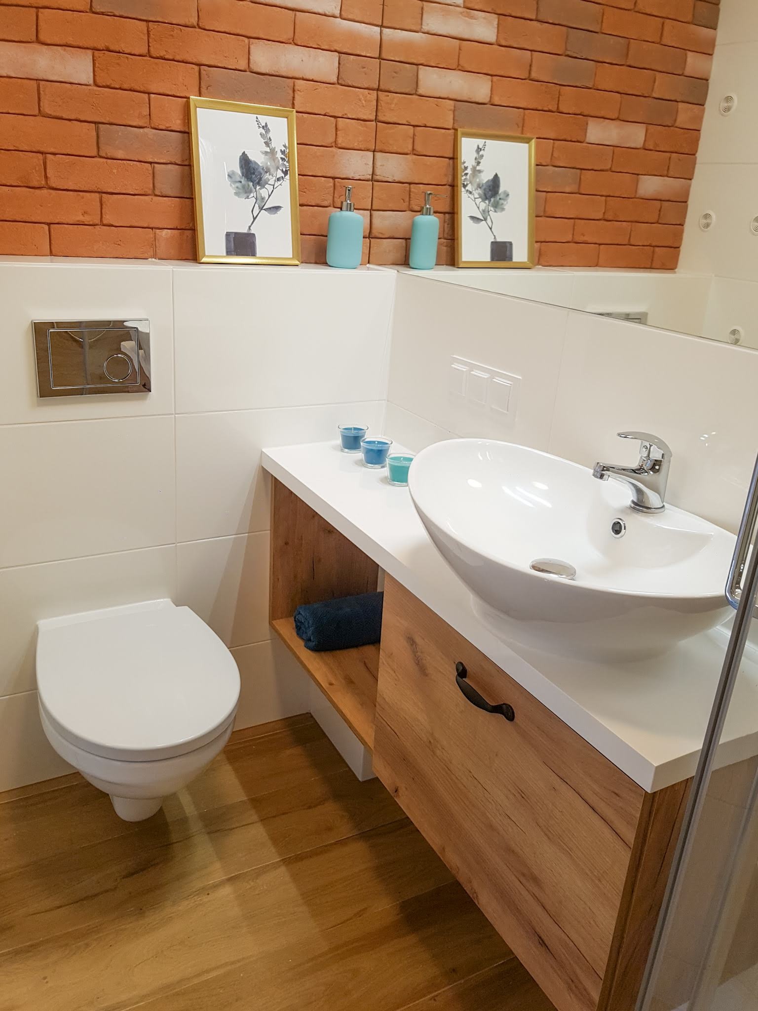 Nowoczesna łazienka z umywalką nablatową, drewnianą szafką, toaletą i dekoracyjną ścianą z cegły.