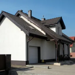 Nowo wybudowany dom jednorodzinny z jasną elewacją, ciemną dachówką i garażem, widoczny z boku w słoneczny dzień.