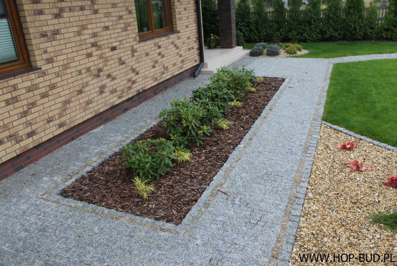 Granitowa ścieżka z obrzeżem i rabata z korą i roślinami przy domu z cegły, widok z góry. Elementy dekoracyjne z kamienia i żwiru.