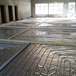 TopInstal Mariusz Wiśniewski - Rozłożona instalacja ogrzewania podłogowego w jasnym, surowym wnętrzu, widoczne pętle rur na folii izolacyjnej, przygotowane do zalania wylewką.