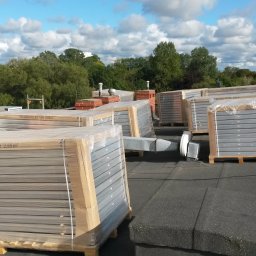 TopInstal Mariusz Wiśniewski - Solarne kolektory 2.65m² na dachu budynku komercyjnego, przygotowane do montażu, widoczne elementy wentylacji i kominy w tle.