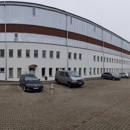 TopInstal Mariusz Wiśniewski - Duży budynek komercyjny z widocznymi instalacjami wentylacyjnymi na elewacji, zaparkowane samochody na pierwszym planie.