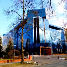 TopInstal Mariusz Wiśniewski - Nowoczesny budynek biurowy z przeszkloną fasadą w Chodzieży, z widocznym otoczeniem miejskim i drzewami bez liści.