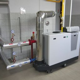 TopInstal Mariusz Wiśniewski - Nowoczesny, biały piec grzewczy De Dietrich z chromowanym kominem i izolowanymi rurami z manometrami w kotłowni wyłożonej kafelkami.