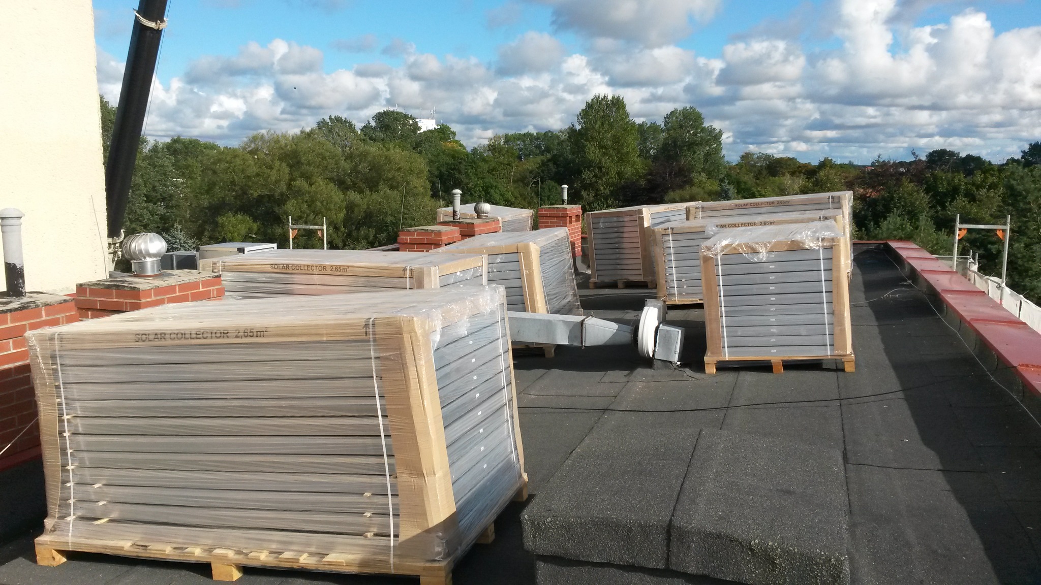 Solarne kolektory 2.65m² na dachu budynku komercyjnego, przygotowane do montażu, widoczne elementy wentylacji i kominy w tle.