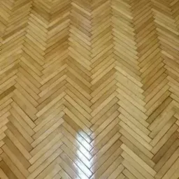 Parkiet ułożony w jodełkę z widocznym odbiciem światła, ukazujący naturalny odcień drewna i precyzję wykonania. Klasyczny wzór podłogi.