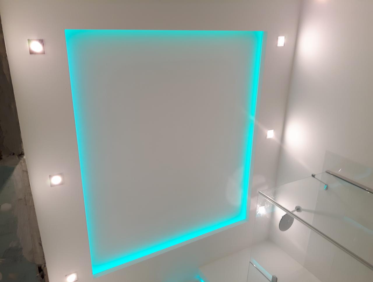 Nowoczesna łazienka z podświetlanym na turkusowo sufitem podwieszanym i punktowym oświetleniem LED, widoczny fragment kabiny prysznicowej.