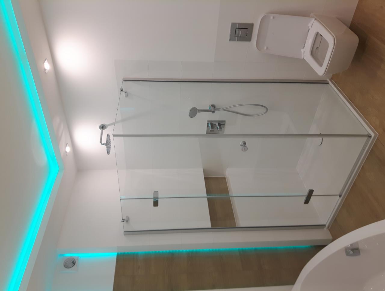 Nowoczesna łazienka z kabiną prysznicową typu walk-in, podświetleniem LED w kolorze turkusowym na suficie i pod kabiną, oraz podwieszaną toaletą.