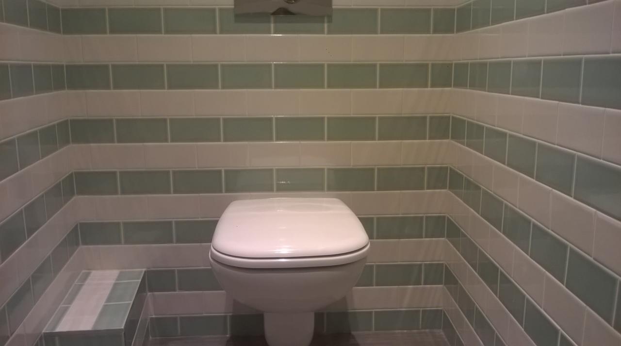 Toaleta wisząca w łazience wyłożonej zielono-białymi płytkami w poziomym wzorze. Widoczna również mała półka z płytek.