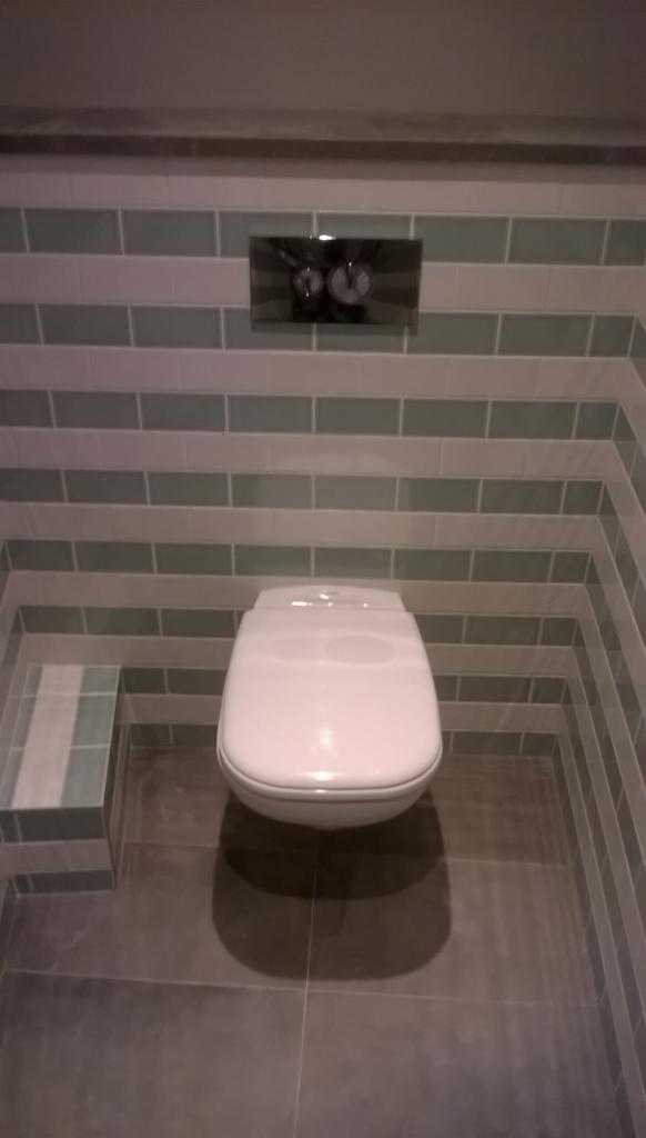 Nowoczesna toaleta podwieszana z mozaiką w odcieniach szarości i zieleni, widok z przodu. Uwagę zwracają geometryczne wzory płytek i minimalistyczny design.