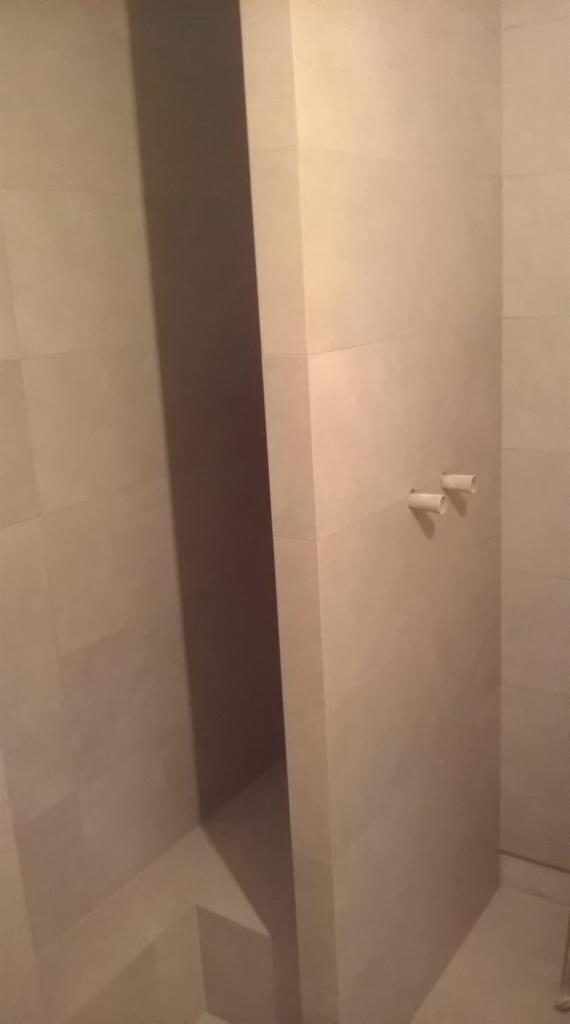 Wykończona łazienka z beżowymi płytkami, widoczne wystające rury instalacji wodnej. Minimalistyczny design i nowoczesne wykończenie.