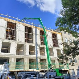 LEGO-BUD Piotr Legędź - Budowa domu z betonu komórkowego w Drużbicach. Widoczna pompa do betonu Putzmeister i pracownik w kamizelce odblaskowej. Budynek w stanie surowym otwartym.