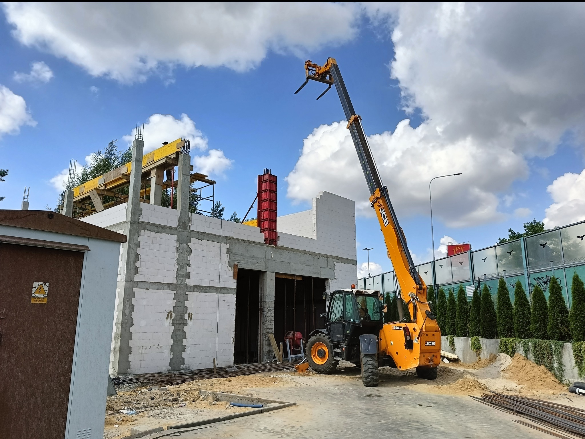 Budowa domu z białych bloczków, widoczny dźwig teleskopowy JCB, szalunki na filarach i stropie. Etap murowania ścian i przygotowania do wylania stropu.