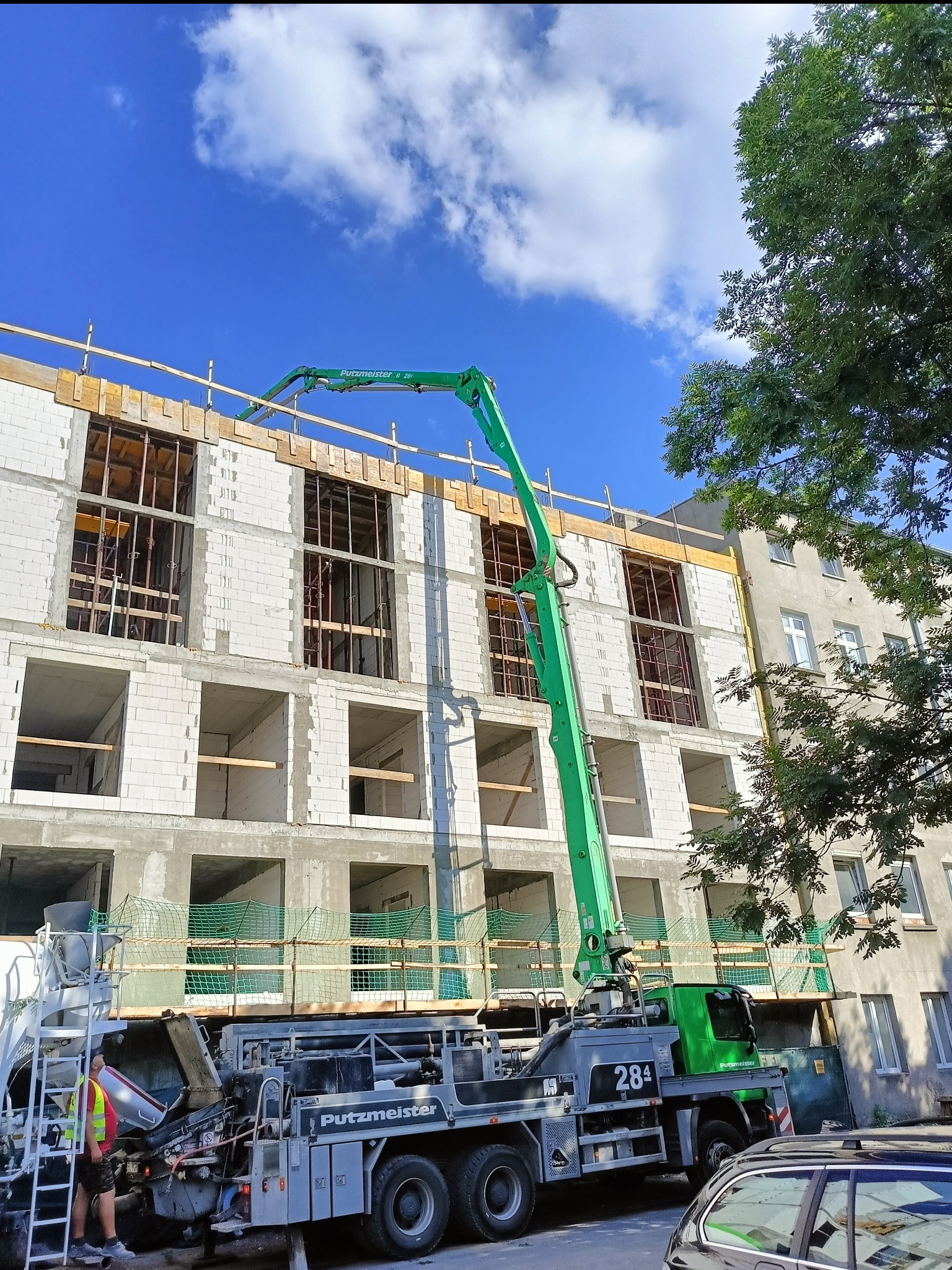 Budowa domu z betonu komórkowego w Drużbicach. Widoczna pompa do betonu Putzmeister i pracownik w kamizelce odblaskowej. Budynek w stanie surowym otwartym.