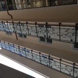 Dwa balkony z czarnymi, metalowymi balustradami z motywem roślinnym i matowym szkłem, widok z dołu na elewację budynku z beżową fasadą i białymi oknami.