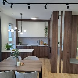 FIRMA REMONTOWO-BUDOWLANA DAREX DARIUSZ NOWICKI - Nowoczesna aranżacja wnętrza: kuchnia z brązowo-białymi szafkami, drewnianym blatem i wyspą, oddzielona od jadalni drewnianą ścianką ażurową, oświetlona czarnymi reflektorami szynowymi i lampą...