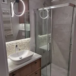 Nowoczesna łazienka w Bydgoszczy: kabina prysznicowa ze szklanymi drzwiami przesuwnymi, umywalka nablatowa na szafce z drewnianymi frontami, oświetlenie LED.