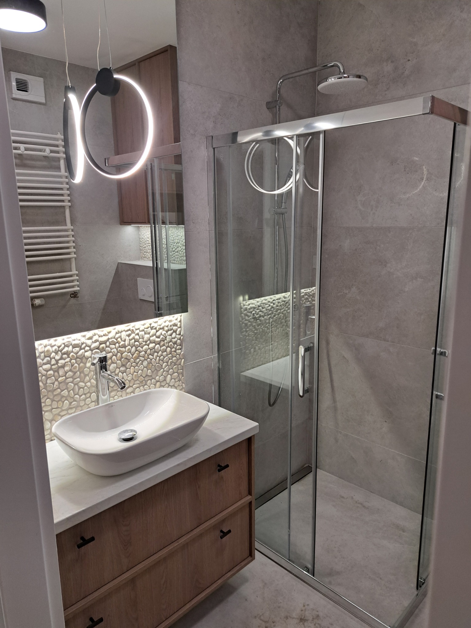 Nowoczesna łazienka w Bydgoszczy: kabina prysznicowa ze szklanymi drzwiami przesuwnymi, umywalka nablatowa na szafce z drewnianymi frontami, oświetlenie LED.