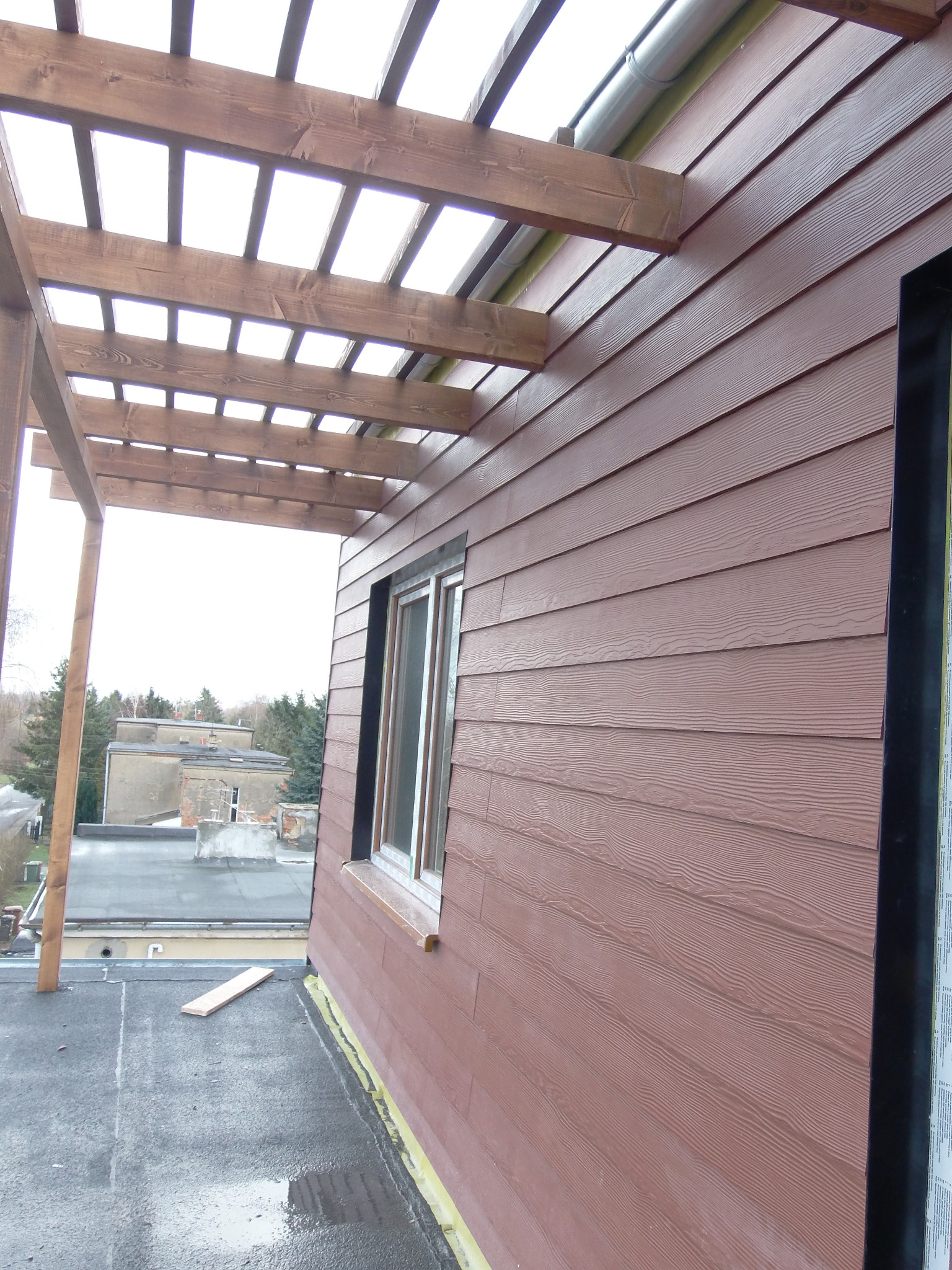 Nadbudowa w Poznaniu z brązową elewacją imitującą drewno i drewnianą pergolą, widok na otoczenie z dachu.