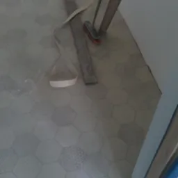 Układanie heksagonalnych płytek podłogowych w trakcie remontu, widoczne narzędzia: wiertarka, listwa pomiarowa i szczotka.