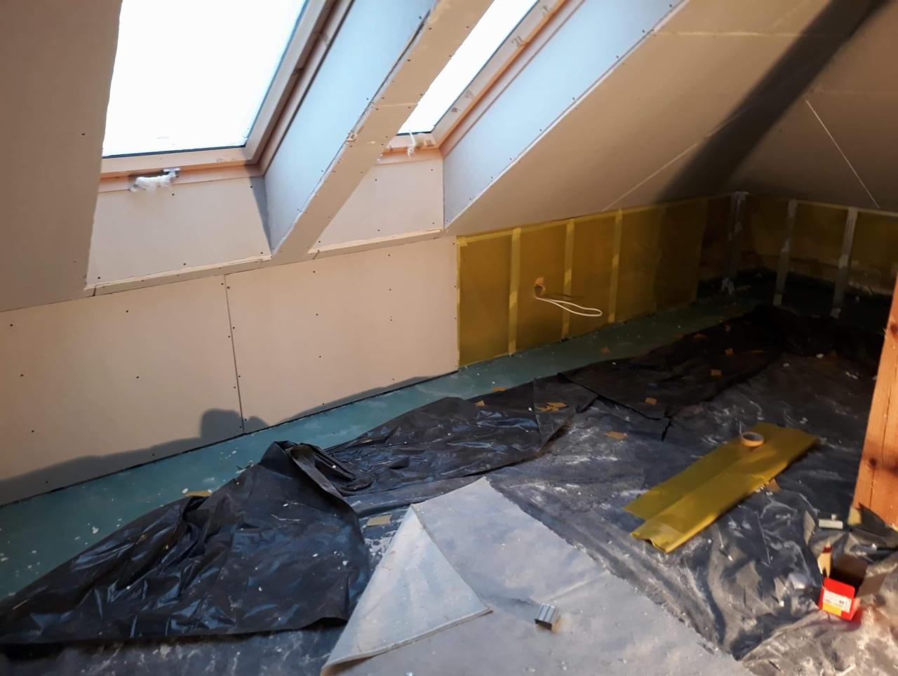 Poddasze w trakcie remontu: ściany obłożone płytami gipsowo-kartonowymi, okna dachowe, folia ochronna na podłodze, widoczne kable elektryczne.