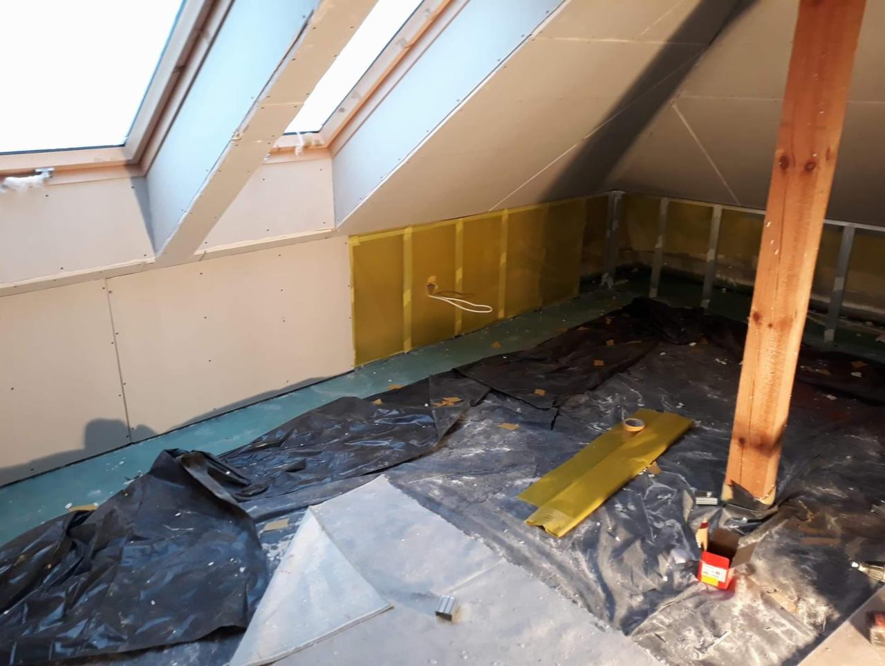 Poddasze w trakcie remontu: izolacja ścian wełną mineralną z widocznymi metalowymi profilami, częściowo obłożone płytami gipsowo-kartonowymi, zabezpieczone folią malarską.