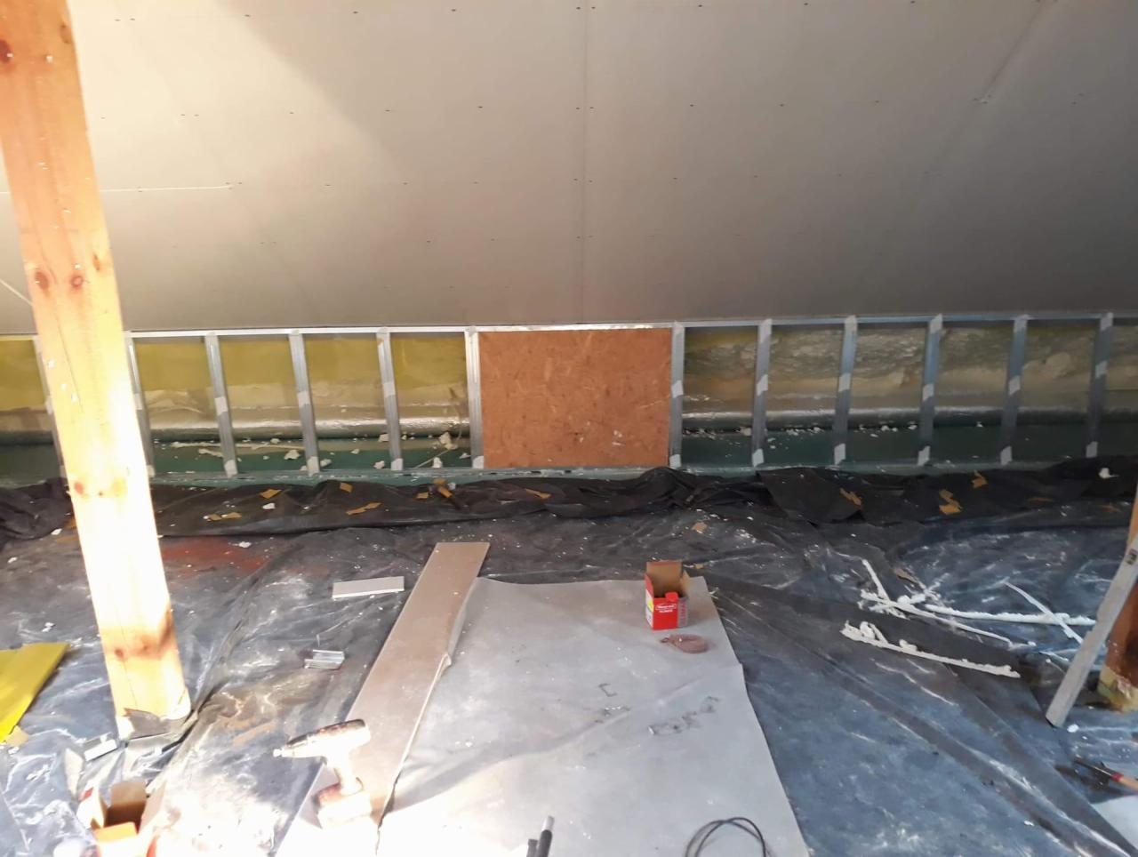 Poddasze w trakcie adaptacji: metalowy szkielet ścian działowych z izolacją, fragment płyty OSB, zabezpieczona folią podłoga z narzędziami i elementami konstrukcyjnymi.