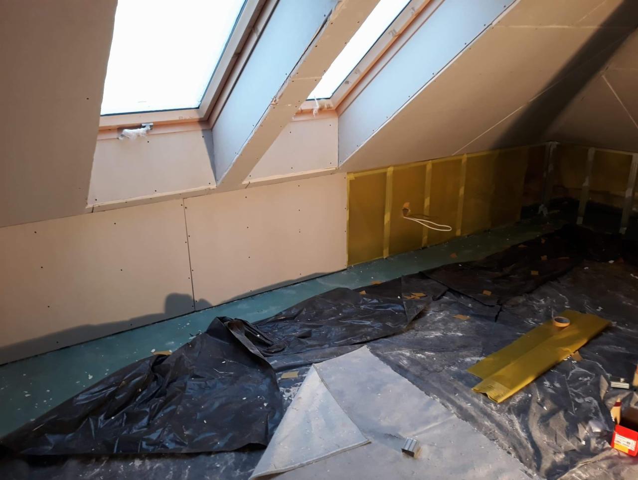 Poddasze w trakcie remontu: widoczne okna dachowe, ocieplenie ścian żółtą folią, płyty gipsowo-kartonowe na ścianach oraz folia ochronna na podłodze.