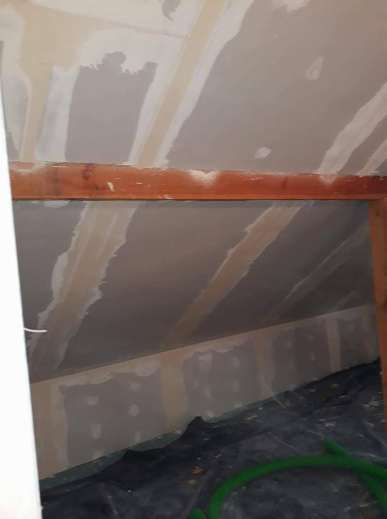 Poddasze w trakcie prac wykończeniowych w Witnicy: widoczne płyty gipsowo-kartonowe na skosach dachu i ścianach, częściowo zaszpachlowane łączenia, drewniana rama okienna i zabezpieczona folią...