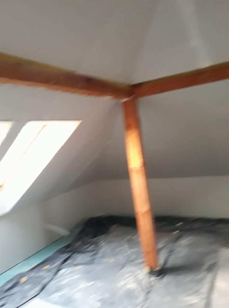 Poddasze w trakcie prac wykończeniowych, widoczne drewniane elementy konstrukcyjne i folia ochronna na podłodze.