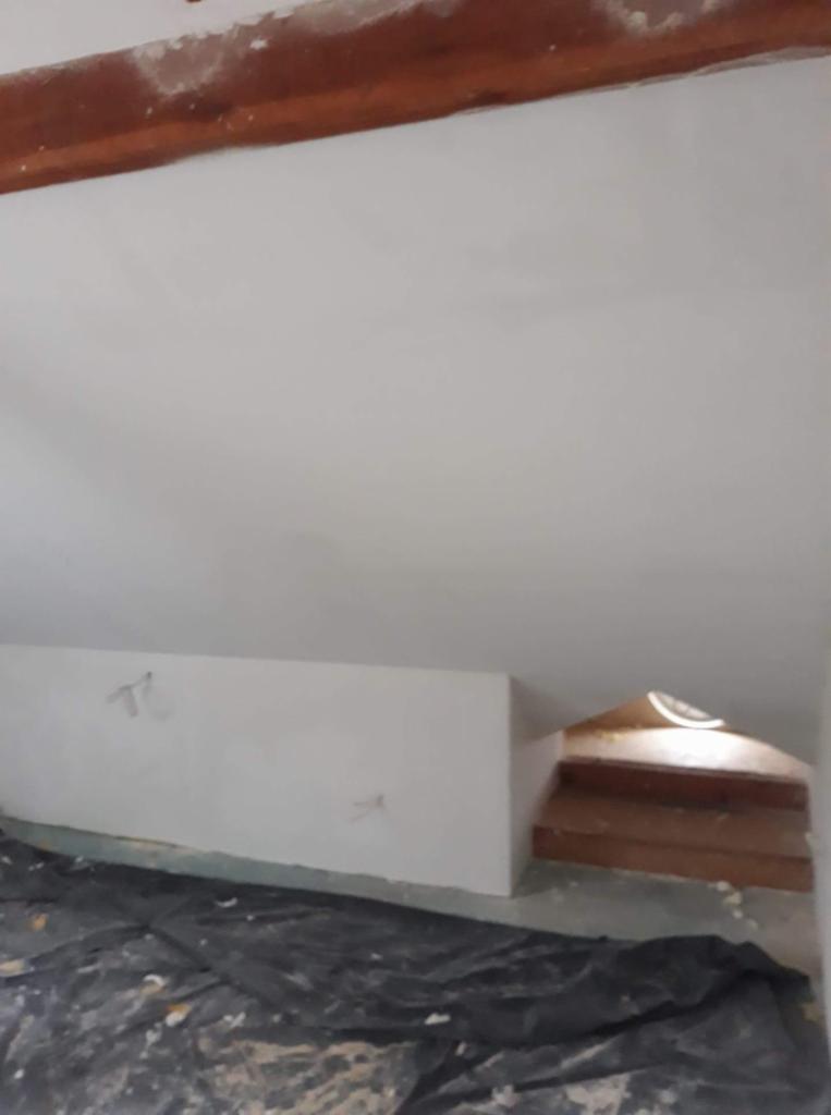 Świeżo pomalowane, białe poddasze z drewnianą belką stropową i zabezpieczoną folią podłogą w trakcie remontu.