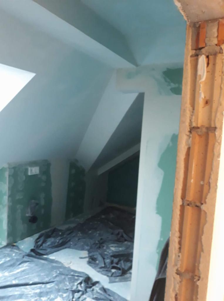 Poddasze w trakcie remontu, ściany pokryte gładzią gipsową, zabezpieczona podłoga folią, widoczna surowa cegła ościeżnicy.