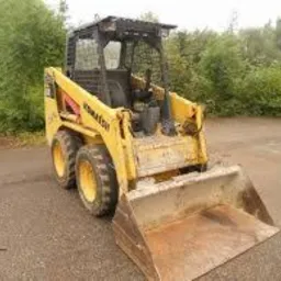 Żółta ładowarka Komatsu na żwirowym placu, z widocznymi śladami użytkowania i lasem w tle. Sprzęt budowlany gotowy do pracy.