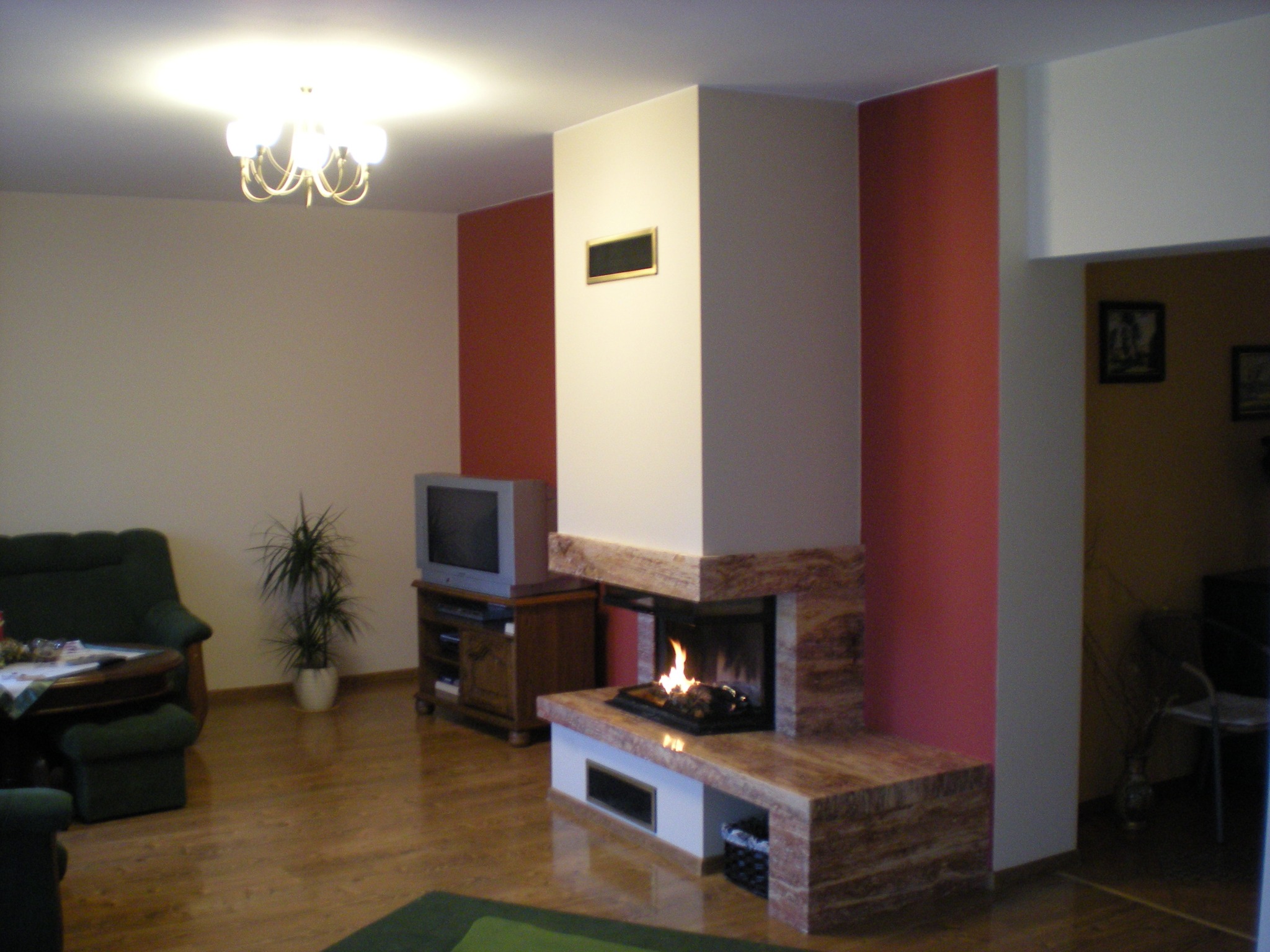 Nowoczesny, marmurowy wkład kominkowy z paleniskiem, w salonie z telewizorem i zielonym dywanem.