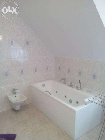 Biała wanna z hydromasażem i bidet w łazience z ukośnym sufitem i jasnymi, wzorzystymi płytkami.