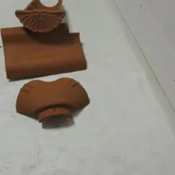 Trzy elementy ceramicznej dachówki RUPP CERAMIKA achat: dachówka podstawowa, ozdobny wiatrownica i zakończenie gąsiora, leżące na jasnej powierzchni.