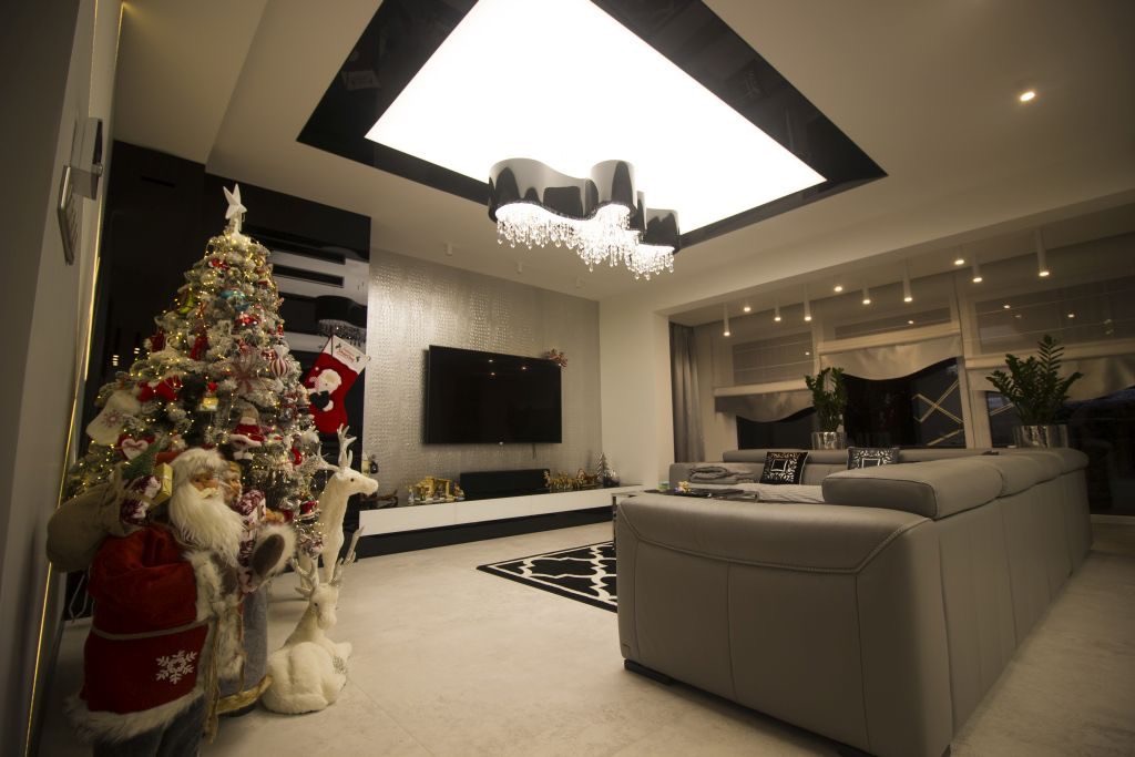 Nowoczesny salon z szarą sofą, choinką z dekoracjami świątecznymi i podświetlanym sufitem z czarną obwódką oraz żyrandolem.