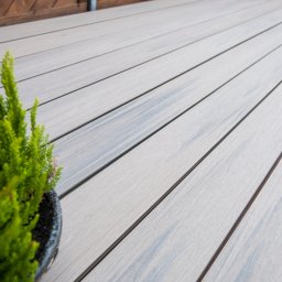 Tarasy z montażem i drewno do Sauny - Jasnoszara deska kompozytowa Gardin ułożona na tarasie, z doniczką z zieloną rośliną w lewym dolnym rogu, widok z bliska pod kątem.